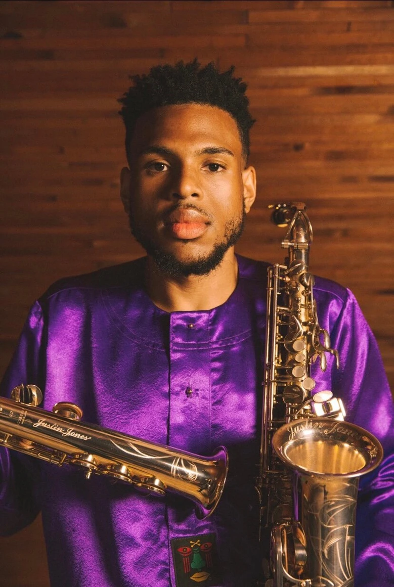 A man in purple shirt holding two saxophones.