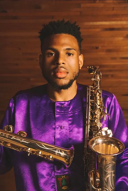 A man in purple shirt holding two saxophones.