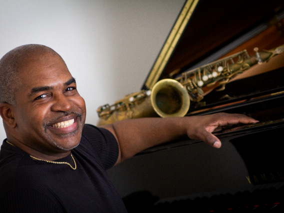 A man smiling and playing the piano with his hand extended out.