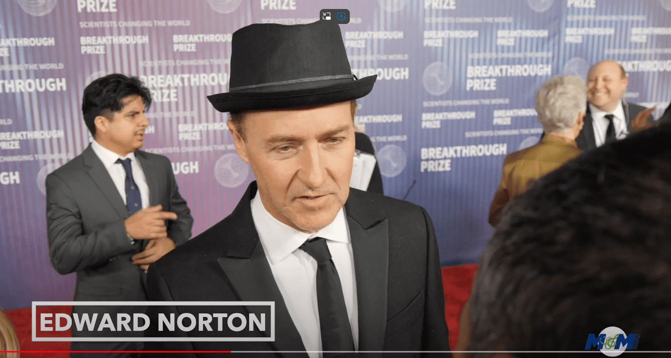 A man in a suit and hat standing on the red carpet.