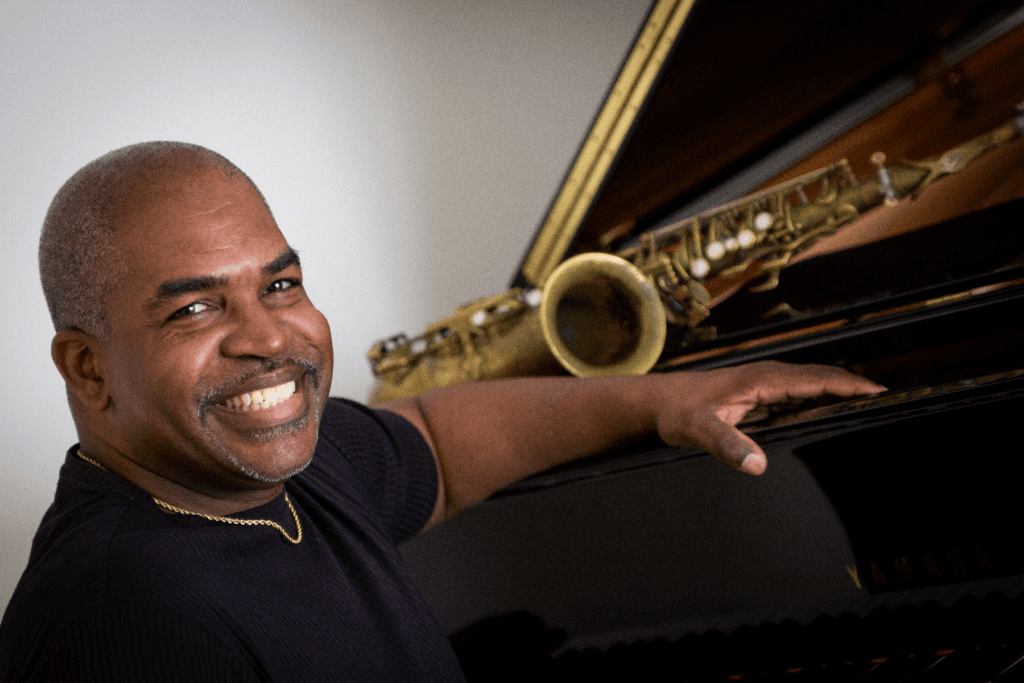 A man smiling and playing the piano with his hand on it.