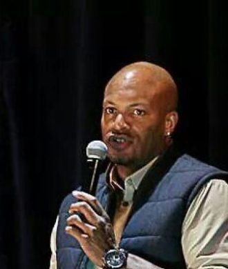 A bald man with a microphone in front of a black background.