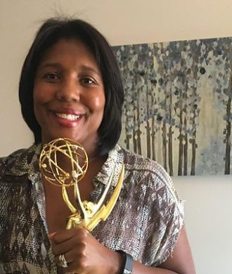 A woman holding up a golden emmy award.